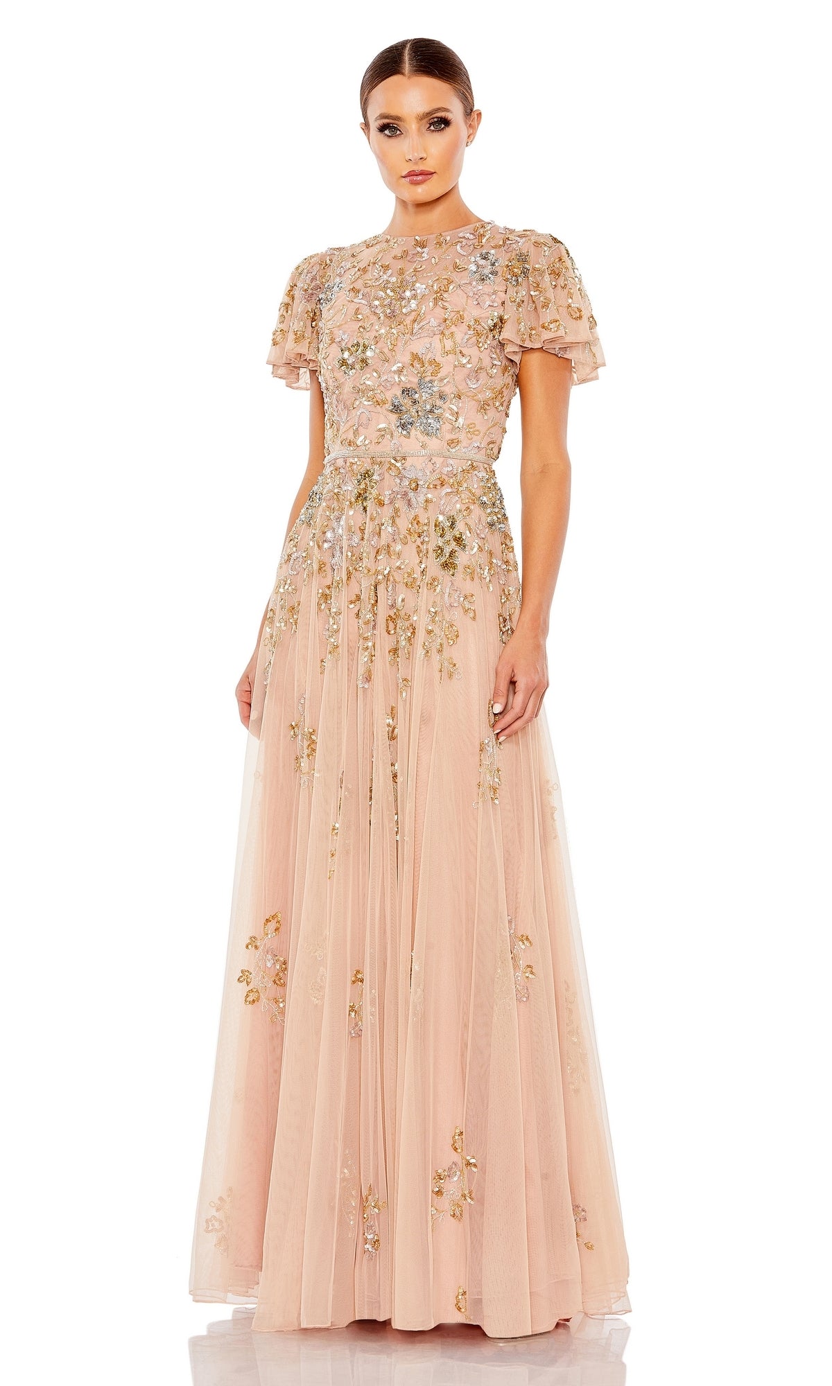 A woman wearing the Mac Duggal 5717 Short Sleeve Beaded Formal Dress, a floor-length blush pink gown with short sleeves and intricate floral embroidery, stands facing forward.